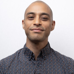 Aashish Portrait smiling with white background, colored dotted shirt, shaved head